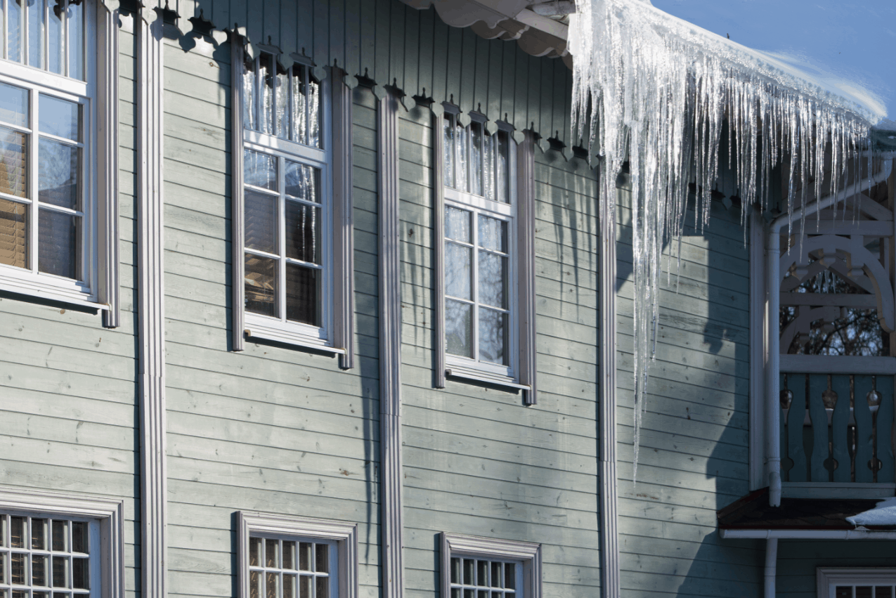 Image shows the side of a home with many large icicles hanging off the roof