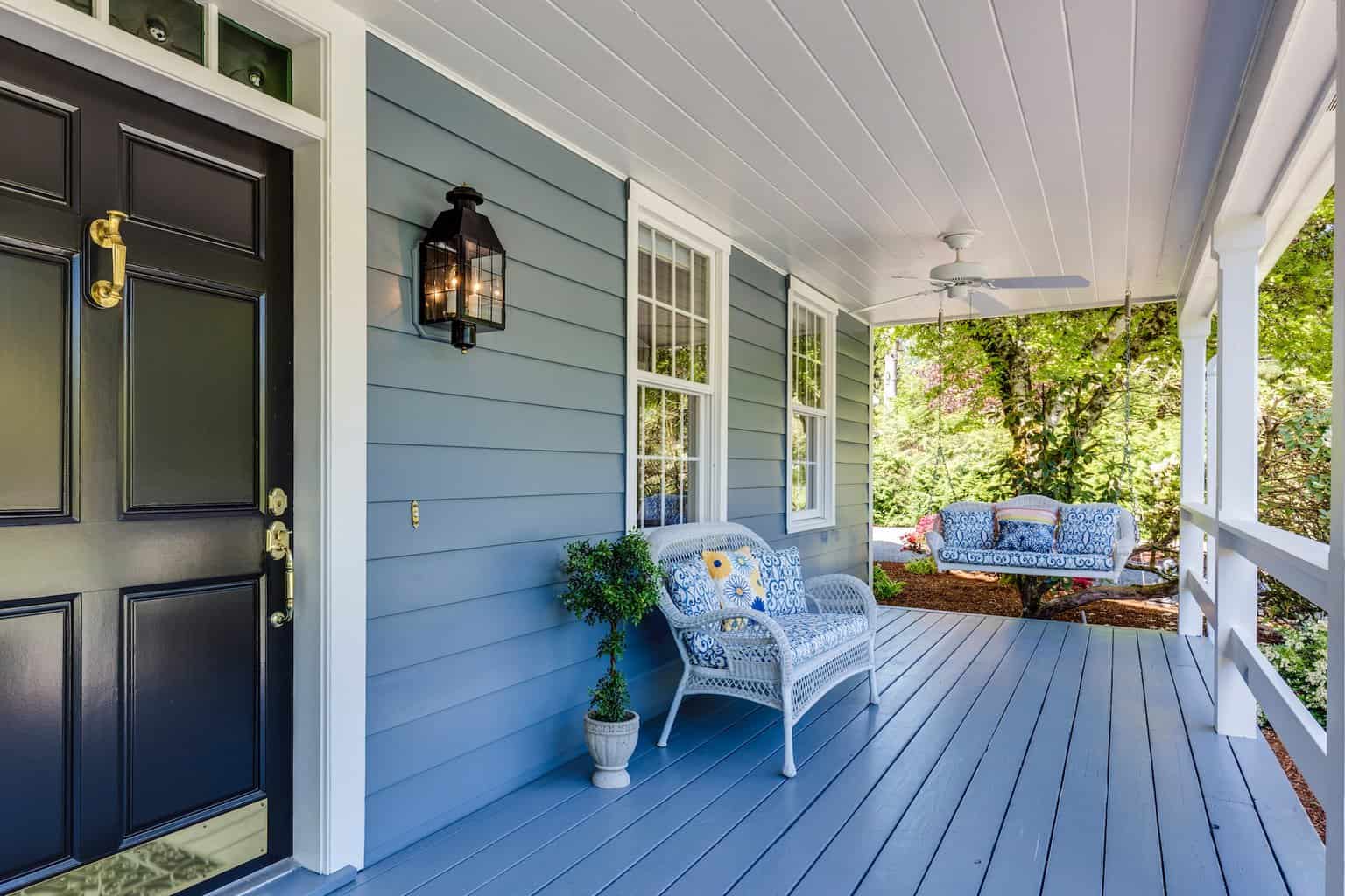 Image shows a front porch on a home with light blue siding and a black door with a white bench