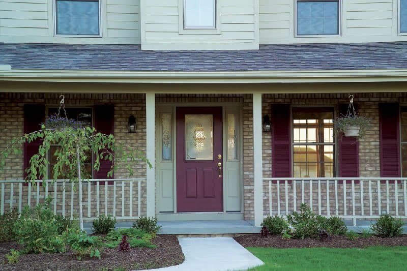 Image shows the exterior of a home with a maroon door and shutters