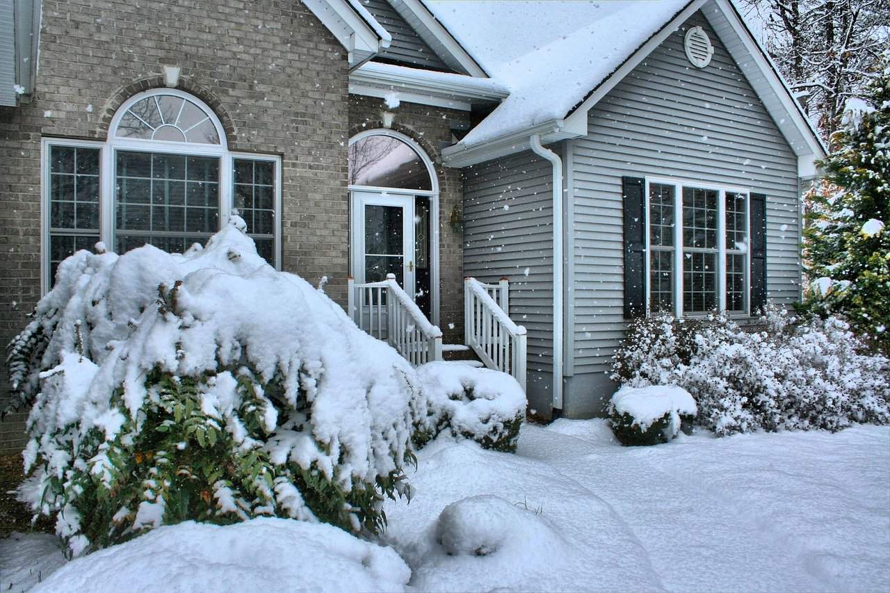 Image shows the outside of a home in winter with snow on the yard and bushes