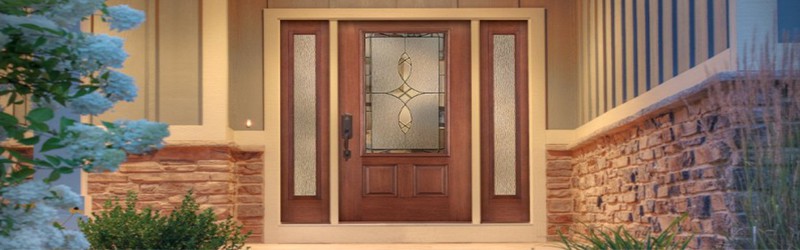 A beautiful woodgrain entry door features two frosted sidelights and a decorative glass pane in the middle. The brown door is at the center of a walkway on a stone brick and wooden home.