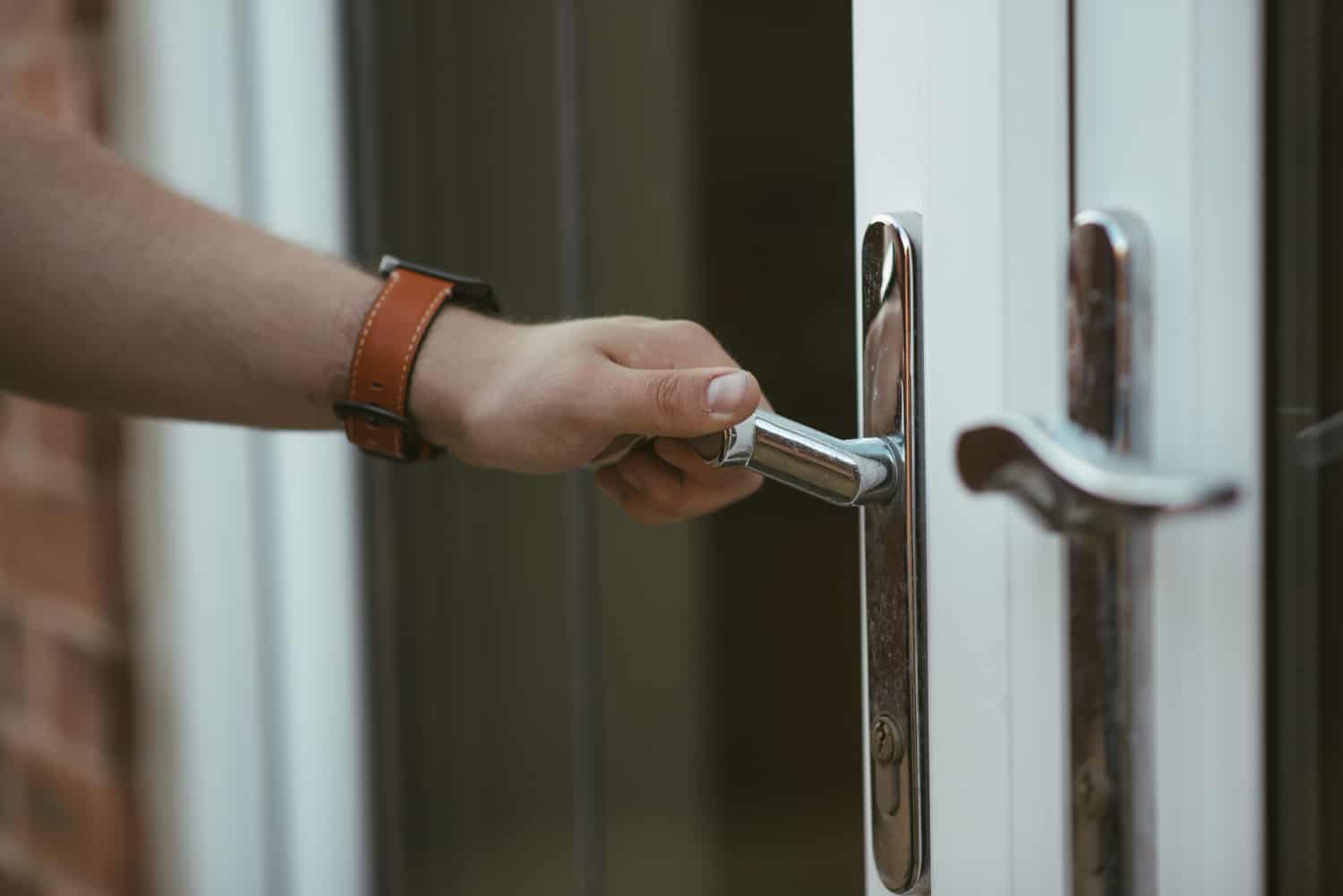 Image shows a hand on a door knob to open a storm door
