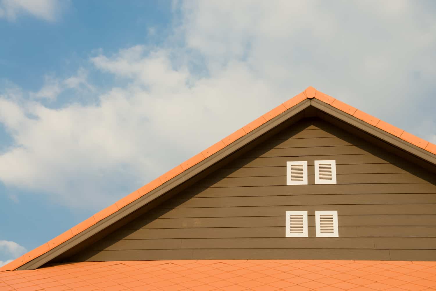 Image shows an orange roof on a brown home with a bright blue background