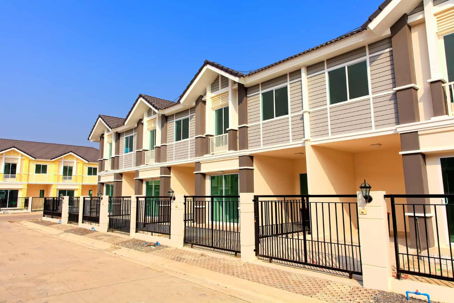 A row of new condos with updated exterior windows, sliding doors, siding, and fences, against a clear blue sky.